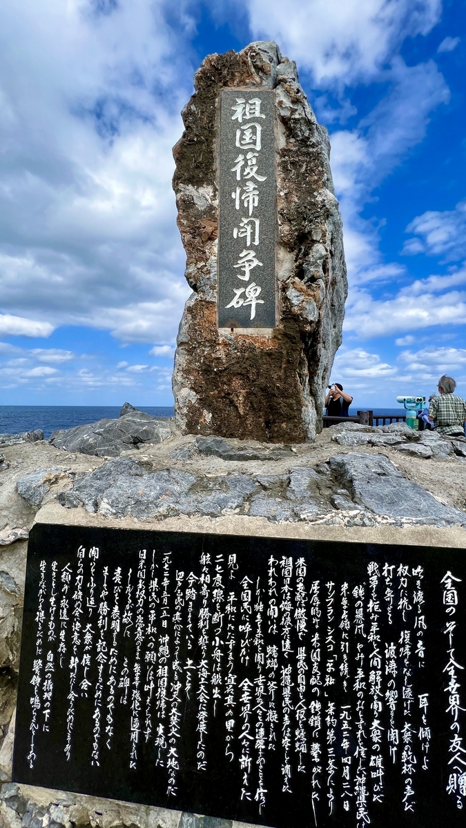青空の下に建つ祖国復帰闘争碑と碑文の刻まれた石碑