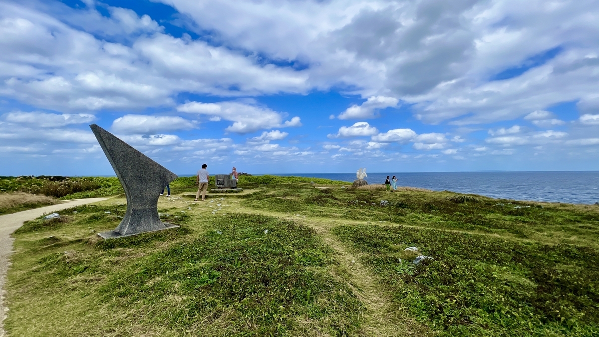開けた草原を進む辺戸岬の遊歩道と彫刻のある風景