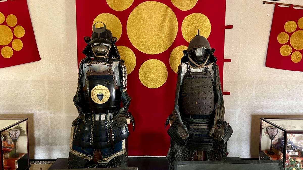 展示室に並ぶ都甲家と荒武家の二領の甲冑と屏風の背景