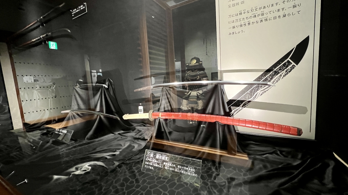 展示ケースに収められた日本刀の展示と背景の解説パネル