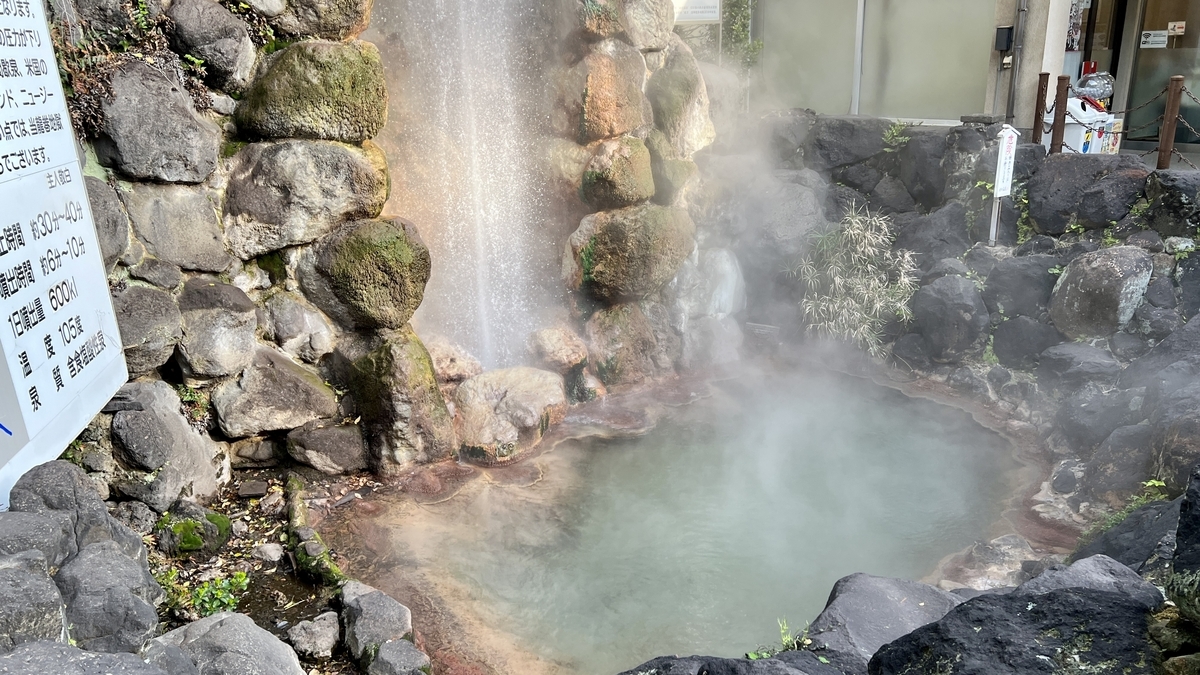 噴出口の横で湯気が立ちのぼる緑がかった湯だまりと岩囲い