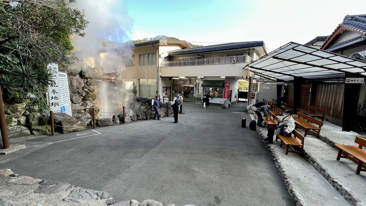 間欠泉の噴出口と売店建物やベンチが見える龍巻地獄の広場全景
