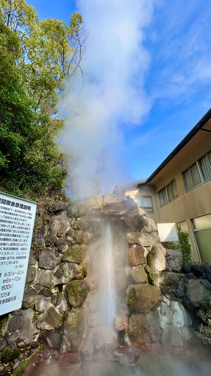 青空を背景に岩組みの噴出口から勢いよく上がる白い噴気