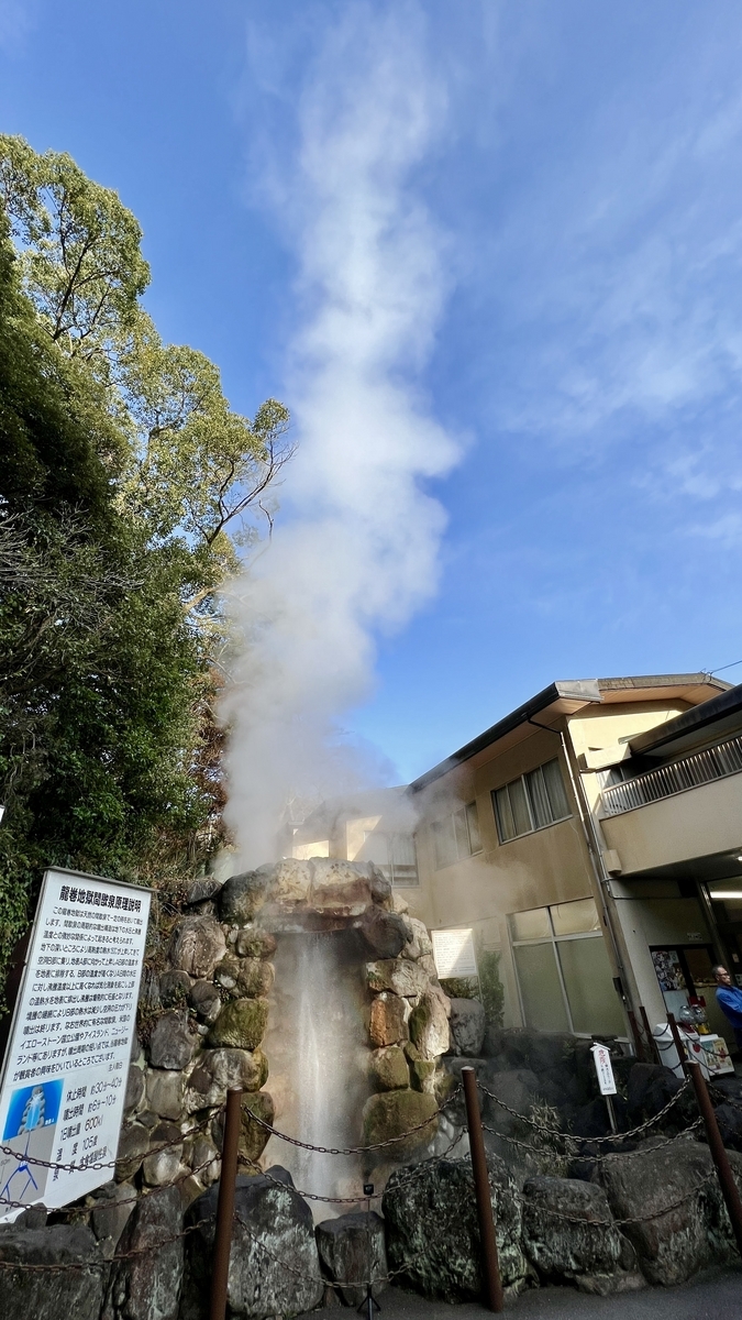 青空に高く立ち上る間欠泉の蒸気と岩組みの噴出口