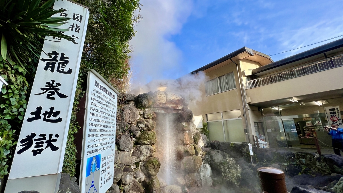 龍巻地獄の立て看板と説明板の横で間欠泉が噴き上がる様子