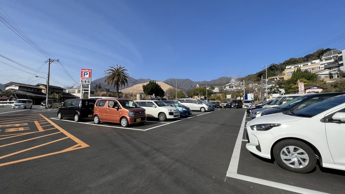 鬼山地獄近くの広い駐車場に車が並ぶ風景と青空