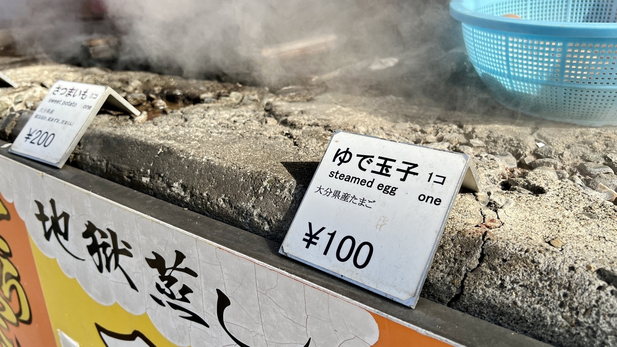 ゆで玉子一個百円と書かれた価格札と湯気が立つ地獄蒸しの釜
