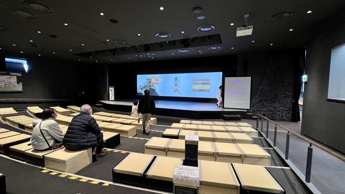 熊本城の映像を上映するわくわく座の劇場と畳座席に座る来館者