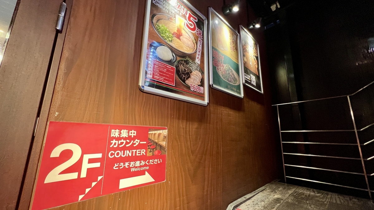 味集中カウンターへ案内する2階への階段案内表示と壁のメニュー写真