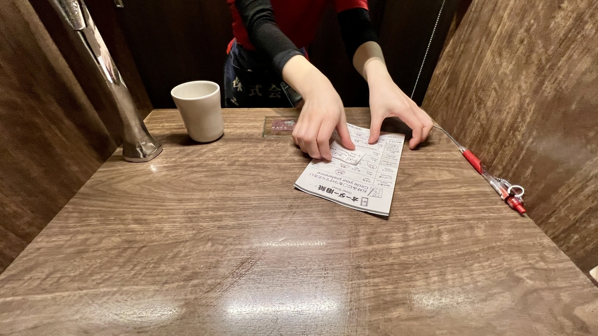 仕切りの席でスタッフにオーダー用紙を手渡して注文完了