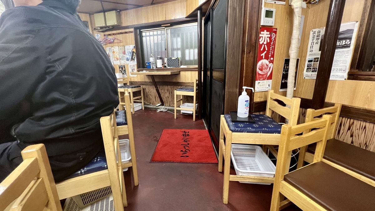 木の椅子が並ぶテーブル席と赤い玄関マットが見える店内通路