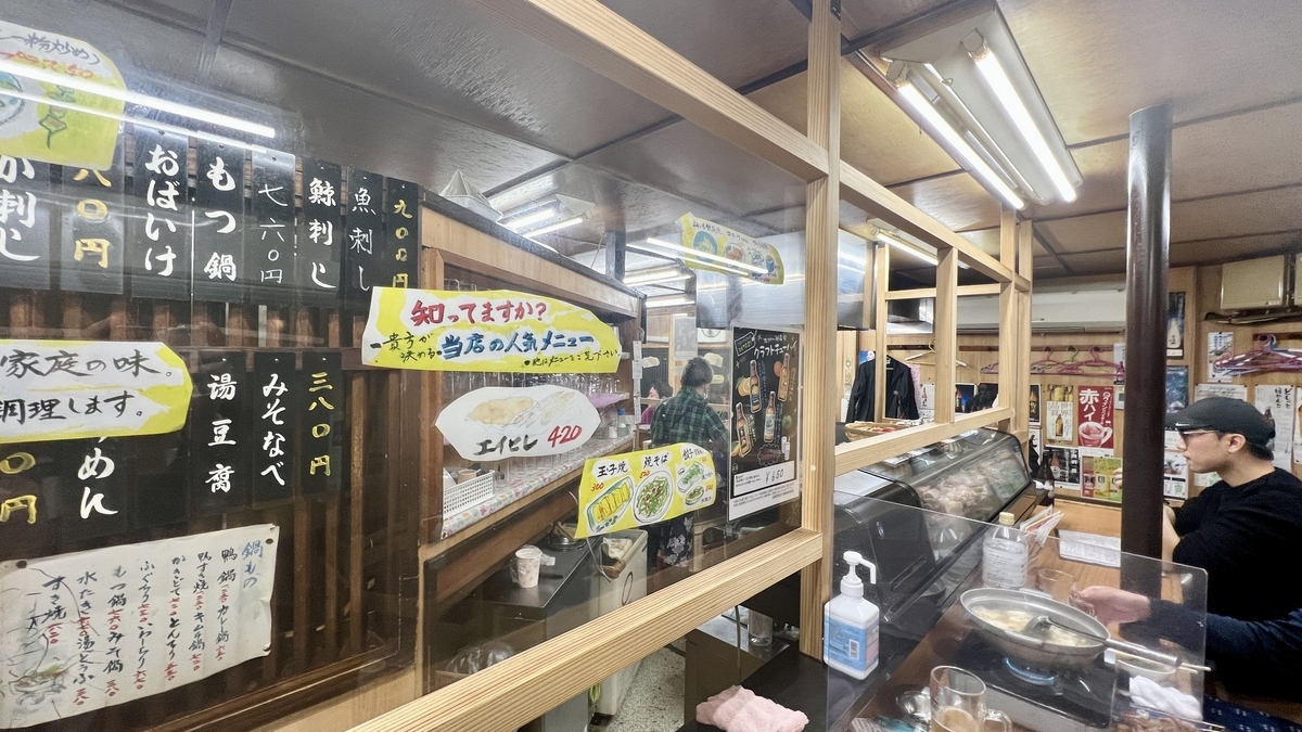 カウンター越しに厨房と短冊メニューが並ぶ木枠の仕切りがある店内
