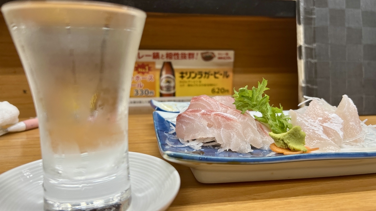 冷酒のグラスと白身魚の刺身盛り合わせが並ぶカウンター席