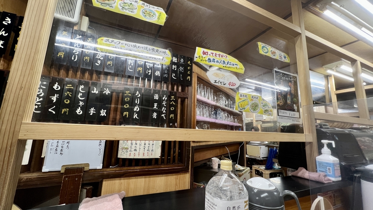 木枠の仕切り越しに見える短冊メニューと厨房がある大衆居酒屋の店内