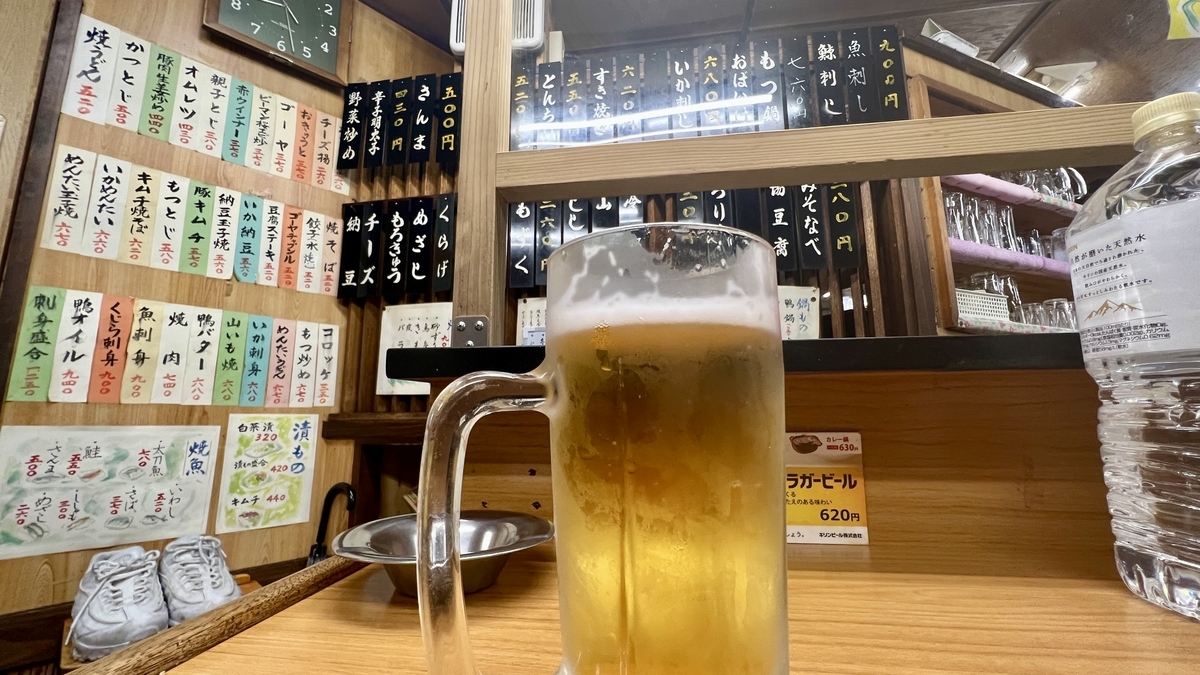 短冊メニューが並ぶ壁を背景にしたカウンター席の生ビールジョッキ