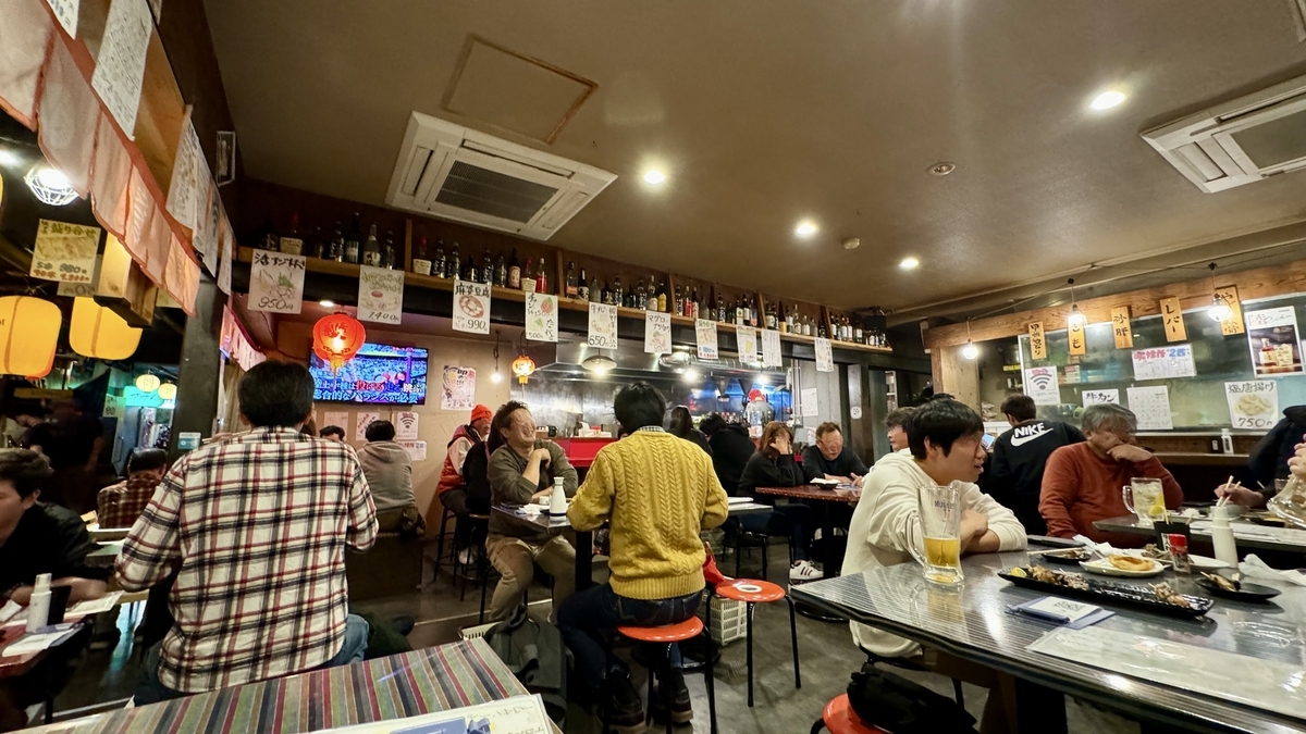 シェアエリアのテーブル席に集う客と壁に並ぶメニュー札