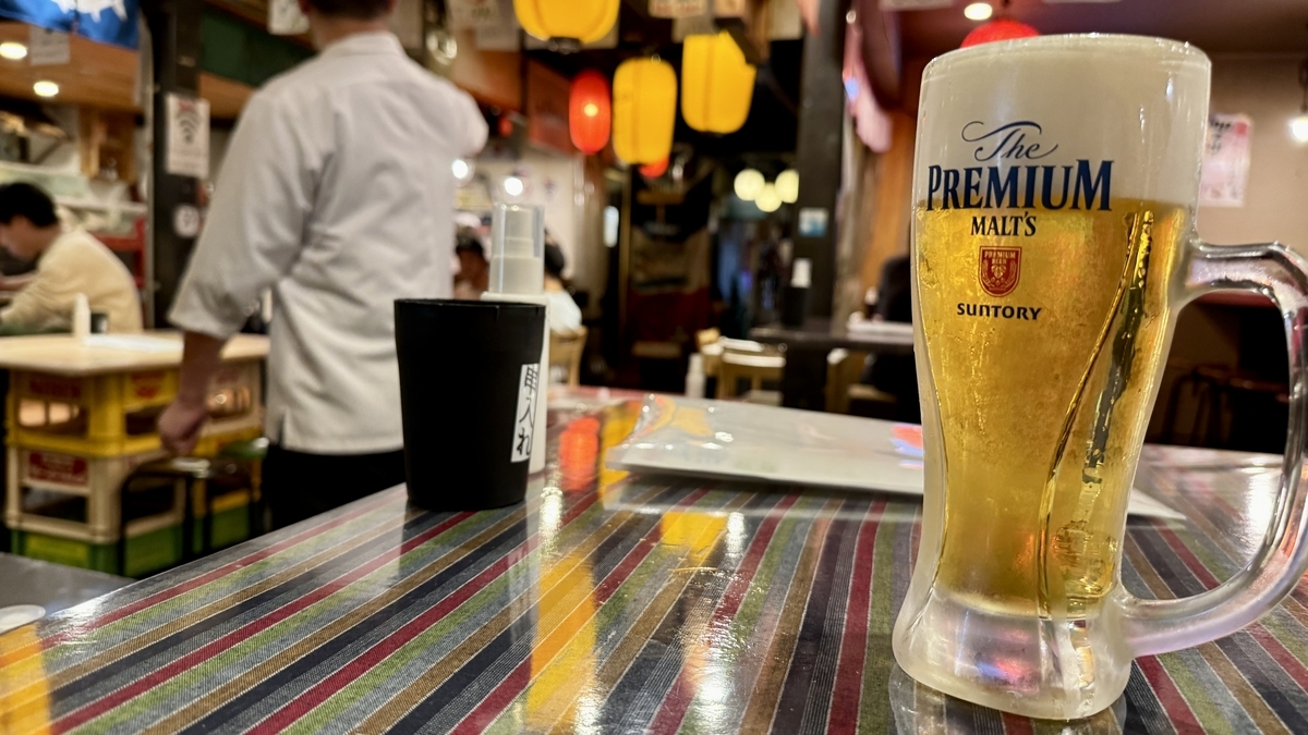 カウンターのテーブルに置かれた生ビールと奥に広がる店内