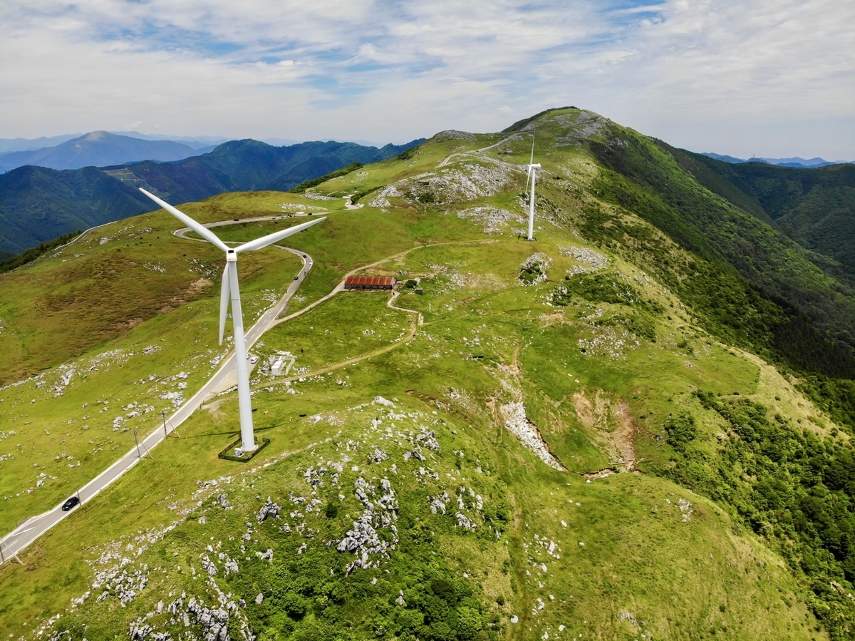 四国カルストの全体を空撮。巨大な風力発電の風車と、ドライブルート。その周辺に草原が広がっている