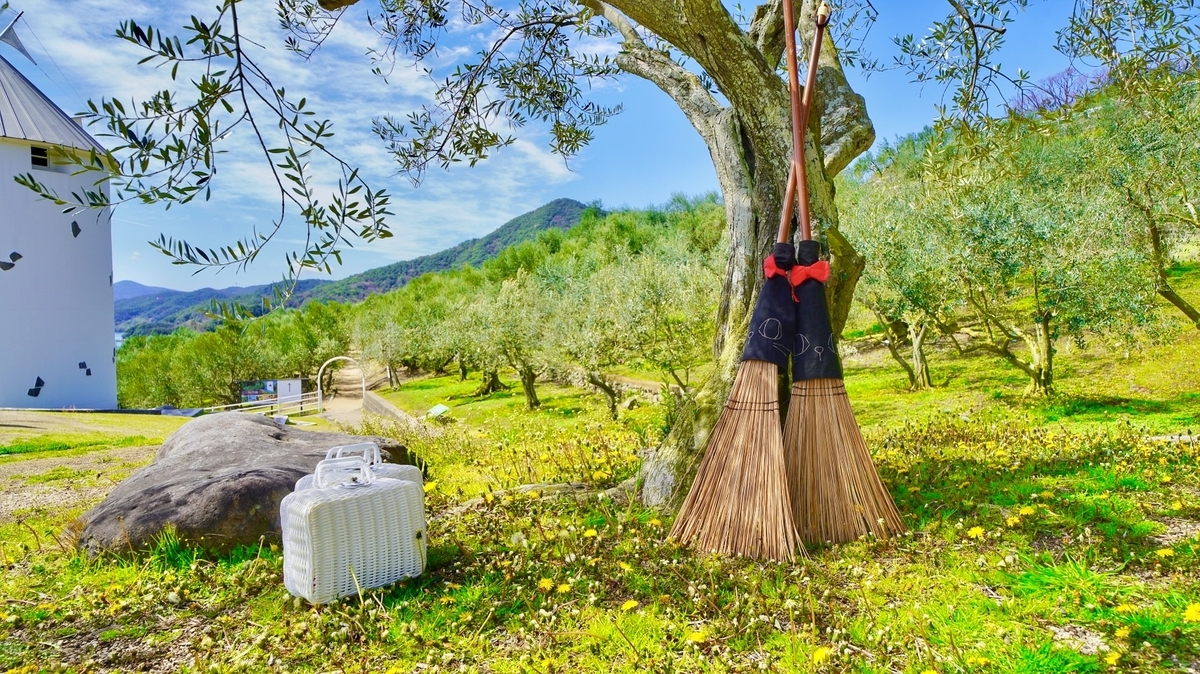 風車を背景にオリーブの木の下でほうきにまたがる人