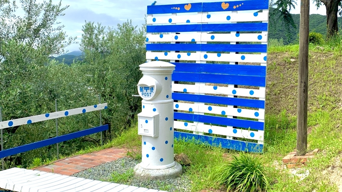 水玉模様の白いポスト 青と白の柵とオリーブの木