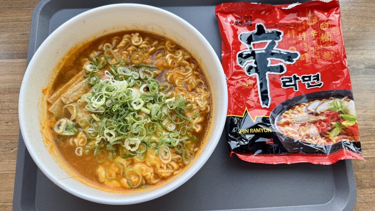 刻みネギをのせた辛ラーメンと商品パッケージ 窓辺のトレーに置かれた完成品
