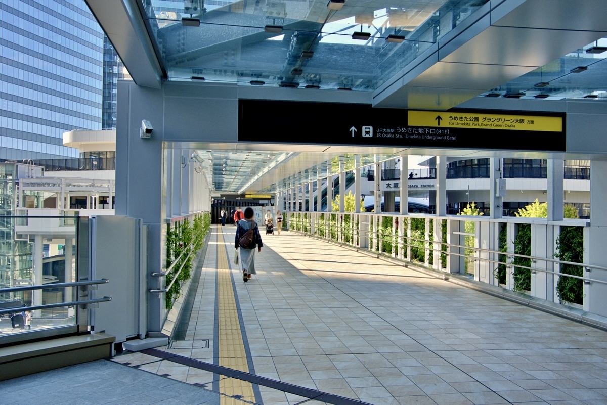 ガラス屋根の連絡通路を通る人と前方にJR大阪駅うめきた地下口方面の案内表示