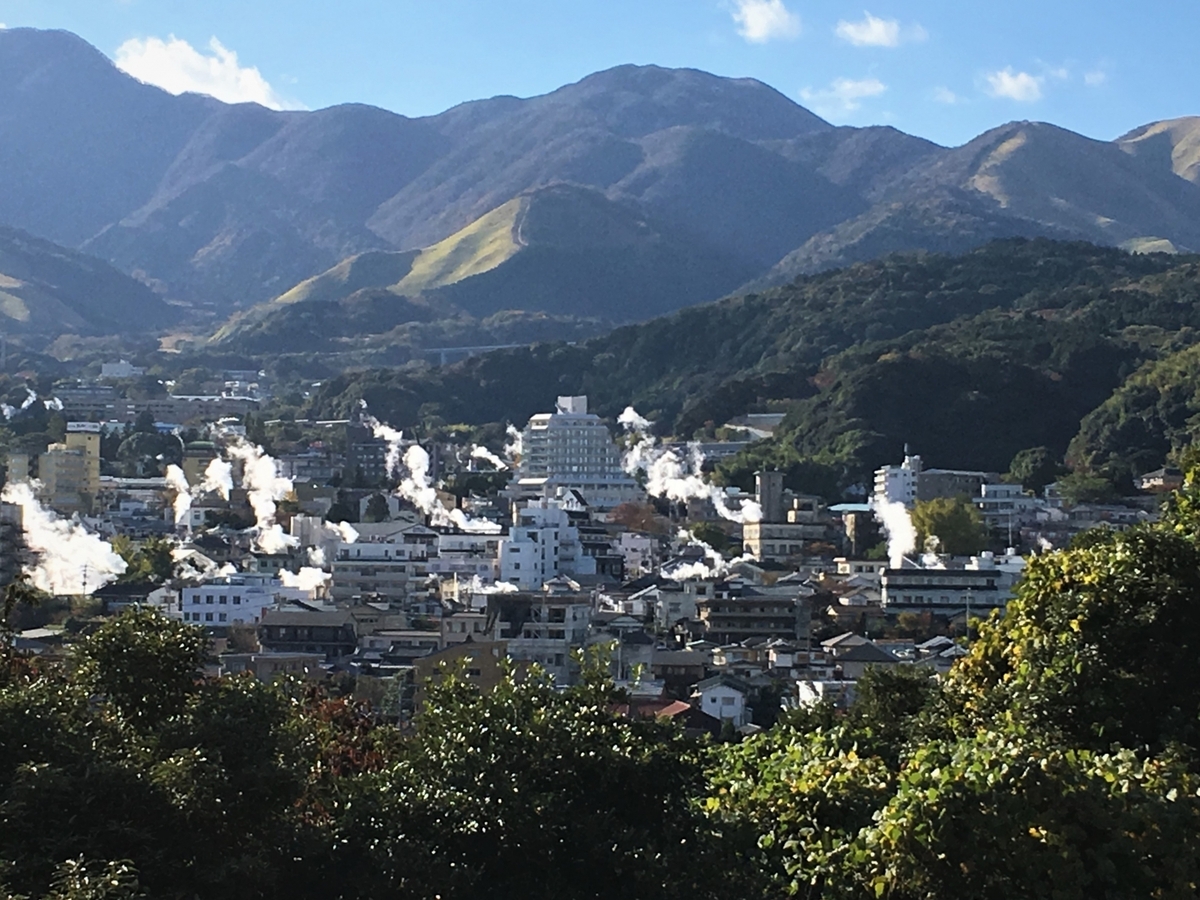 朝の別府市街地に白い湯けむりが立ちのぼり背後に連なる山々が見える眺め