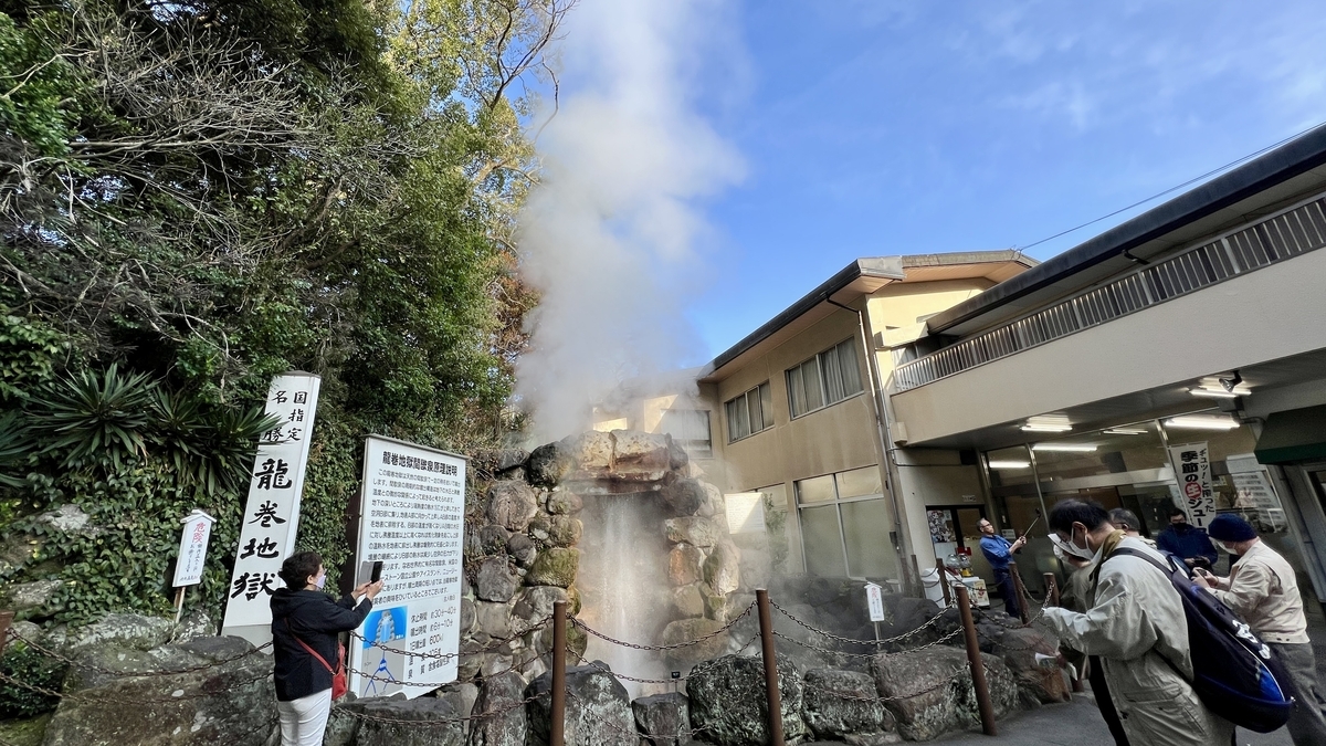 龍巻地獄の噴出口から立ち上る湯けむりと説明看板の前で見学する人々