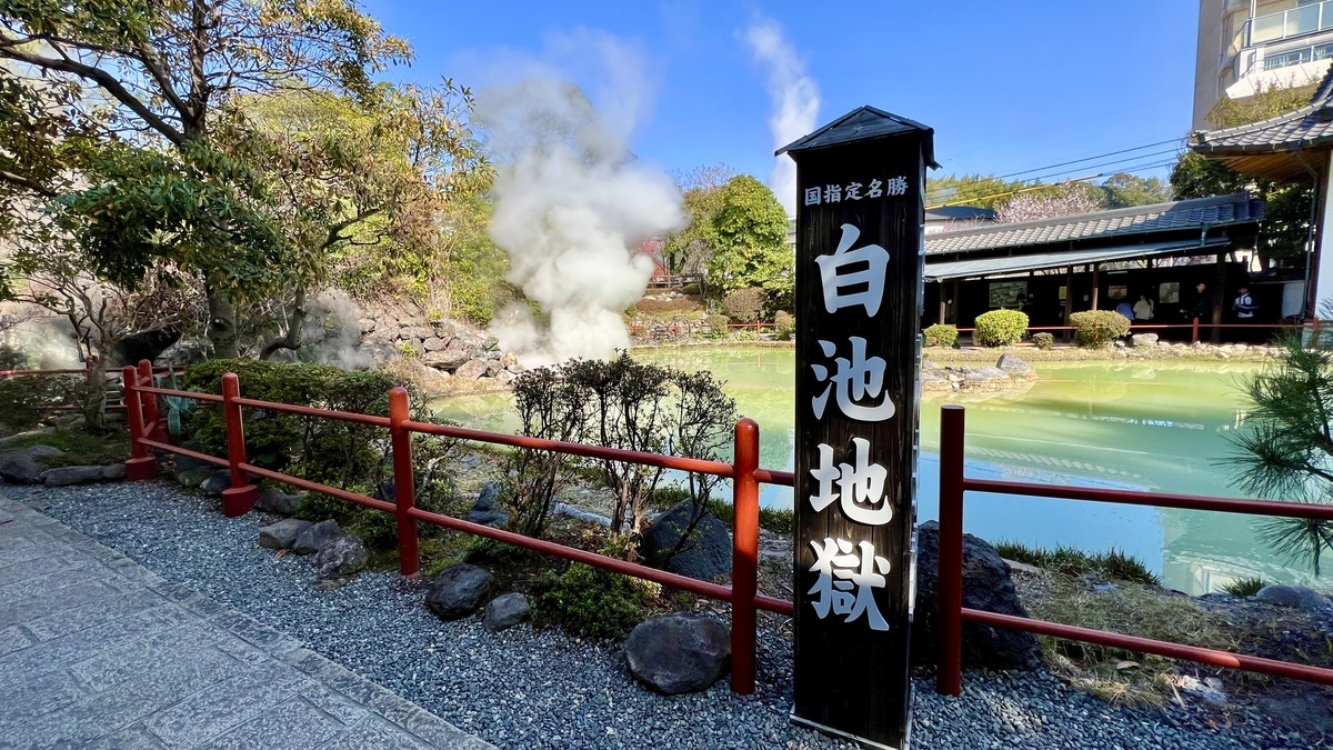 白池地獄の黒い看板と青白く光る温泉池そして湯けむりが立つ庭園の風景