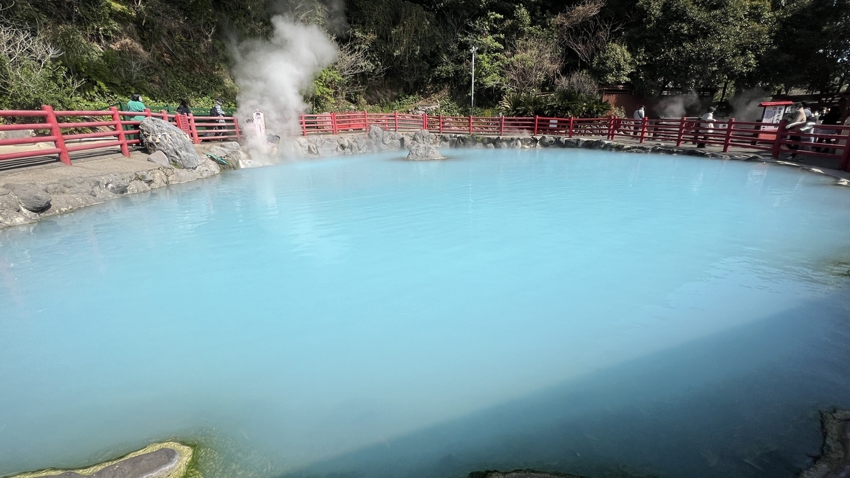 かまど地獄の青く濁った温泉池と赤い柵の遊歩道そして立ち上る湯けむり