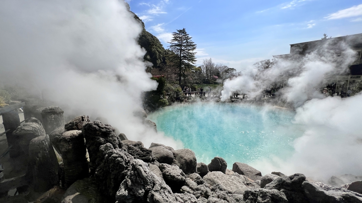 海地獄のコバルトブルーの温泉池を岩場越しに眺め湯けむりが立ち上る景色