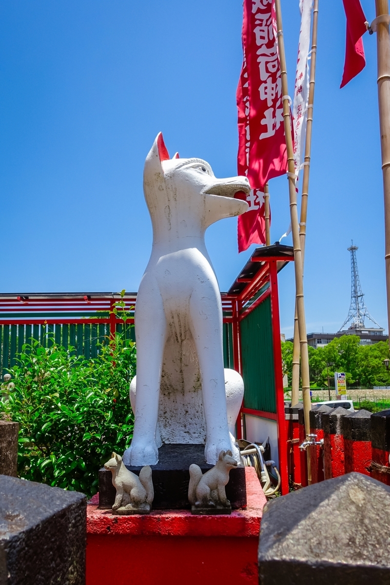 赤い台座に座る白い狐の神使像と子狐
