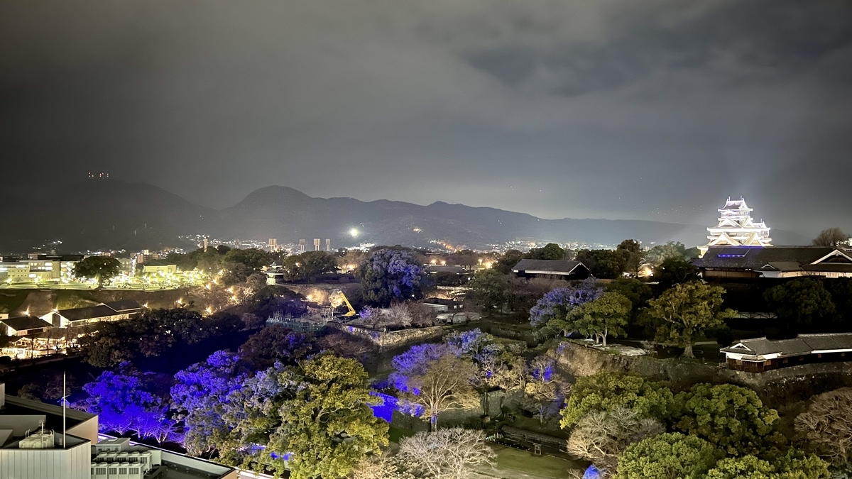 熊本市役所展望台から見た夜の熊本城 天守と城跡の木々がライトアップされ山並みが遠景に広がる