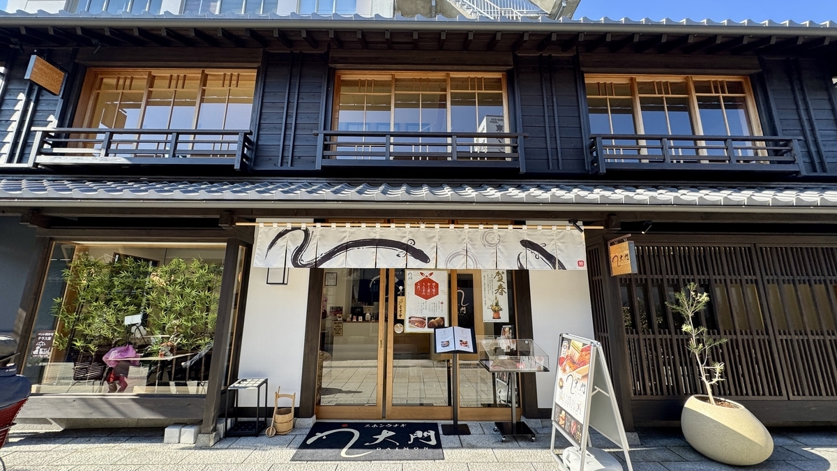 鰻料理店の店先 暖簾と看板の前に料理写真のメニューが並ぶ町屋の外観