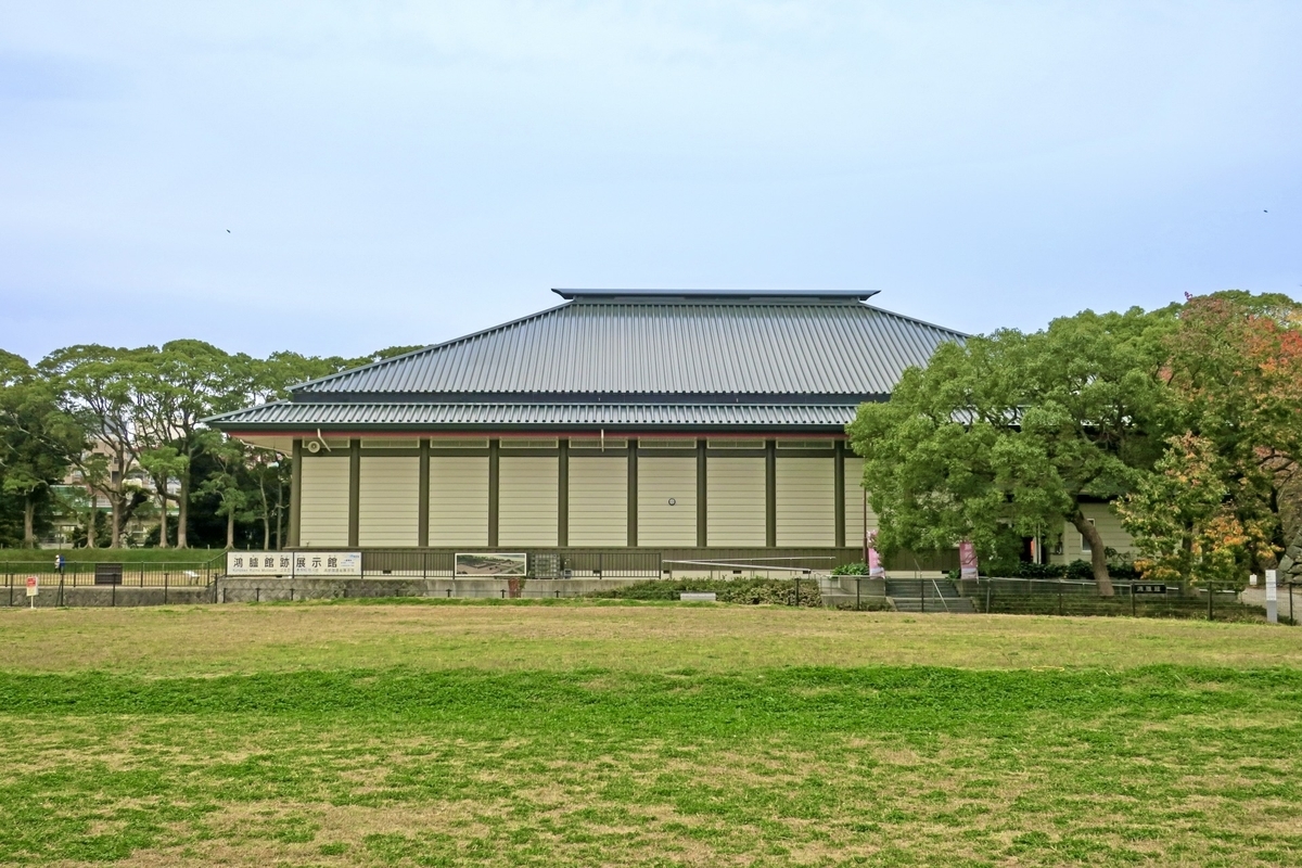 広い芝生広場の奥に建つ鴻臚館跡展示館の切妻屋根の外観