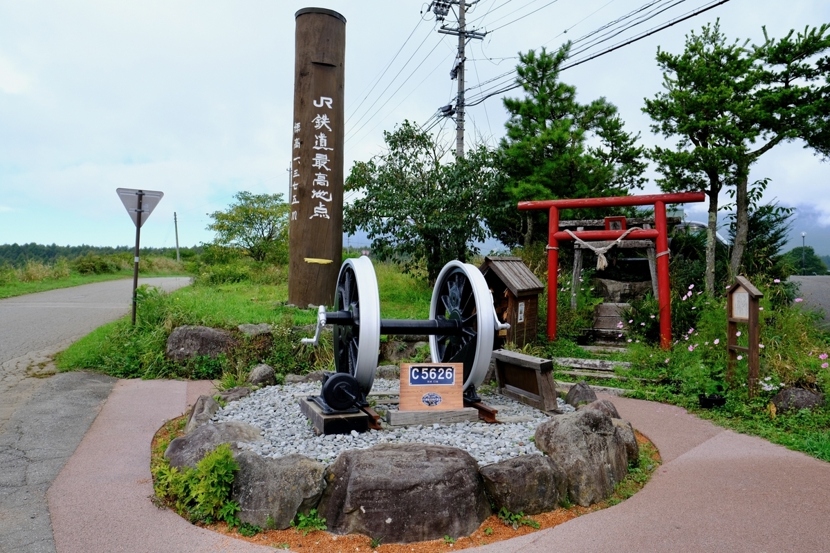 JR鉄道最高地点の木柱と蒸気機関車の車輪を祀る石組みと赤い鳥居が並ぶ鉄道最高地点神社
