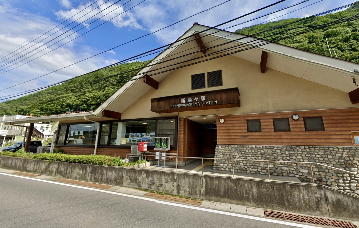 緑の山並みを背にした新島々駅の木造風駅舎と入口の駅名看板