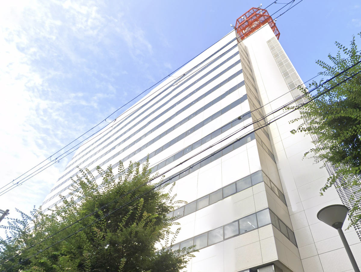 青空に伸びる白い外壁のJR西日本本社ビルと屋上の赤い鉄塔と街路樹