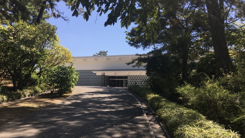 木漏れ日の並木道の奥に建つ白い外壁の大和文華館の外観