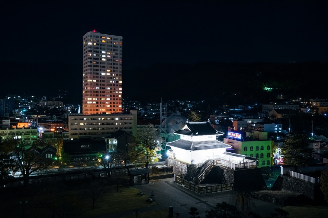 夜の市街地に浮かぶライトアップされた稲荷櫓