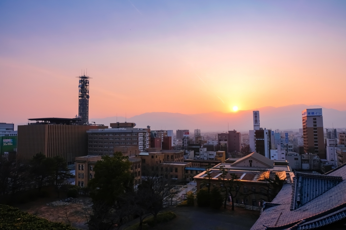 甲府市街地の建物越しに沈む夕日と山並み