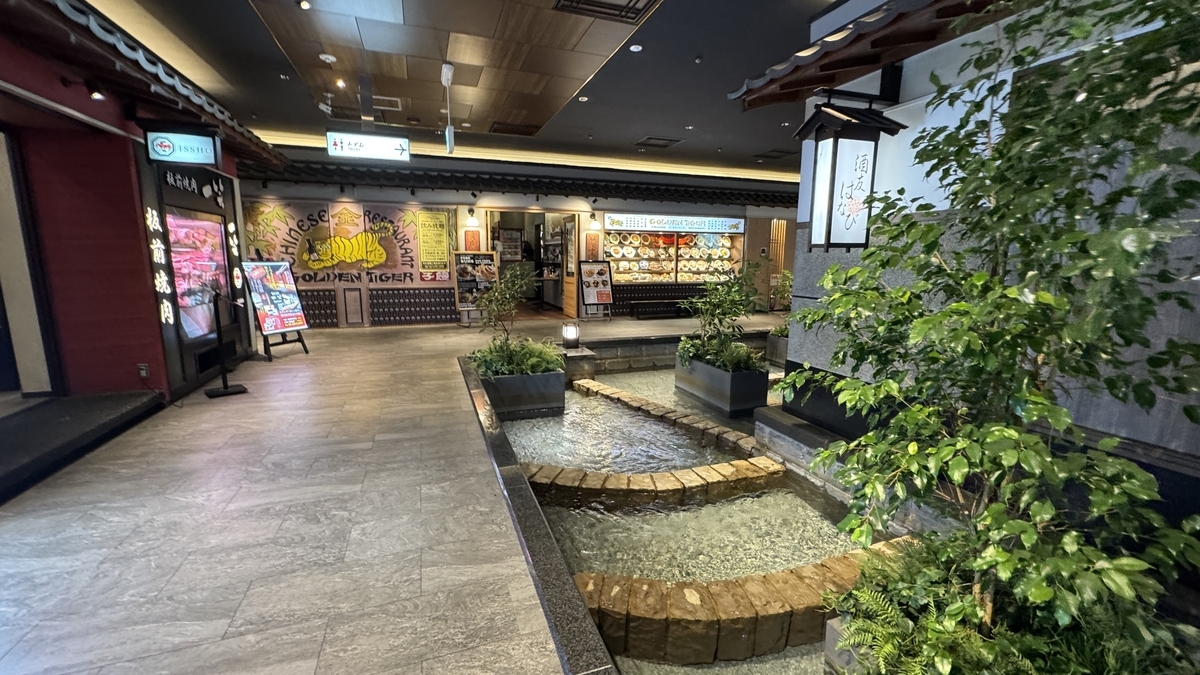 石畳の小さな川と植栽が配置された梅田しばちかの通路と店舗の看板