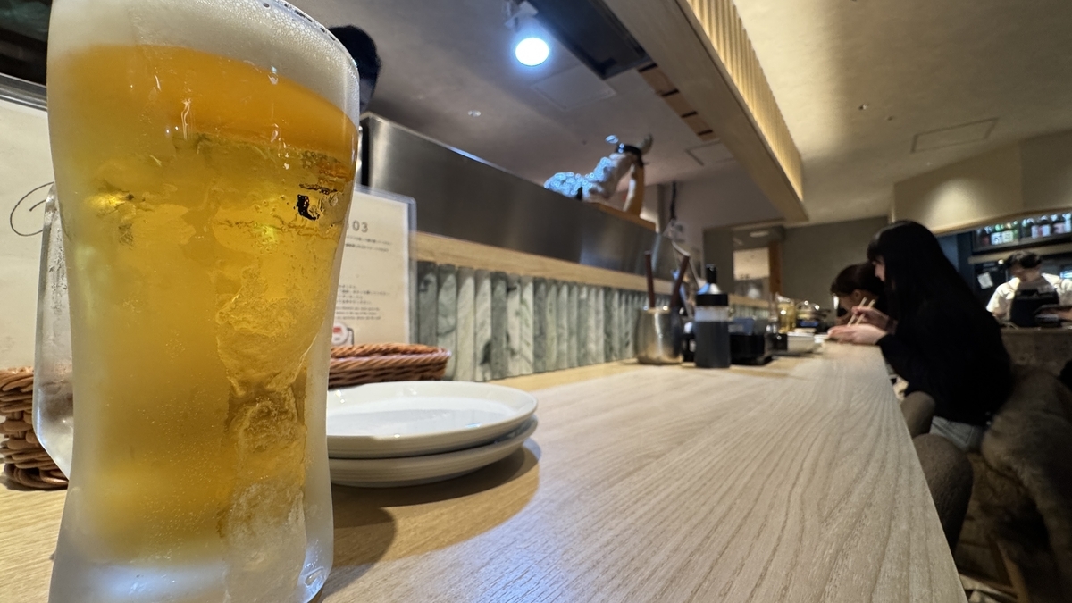 カウンター席に置かれた生ビールと奥に続く居酒屋の店内