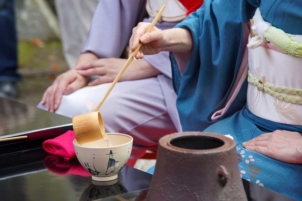 着物の人が柄のある茶碗に柄杓で湯を注ぐ茶道の手元