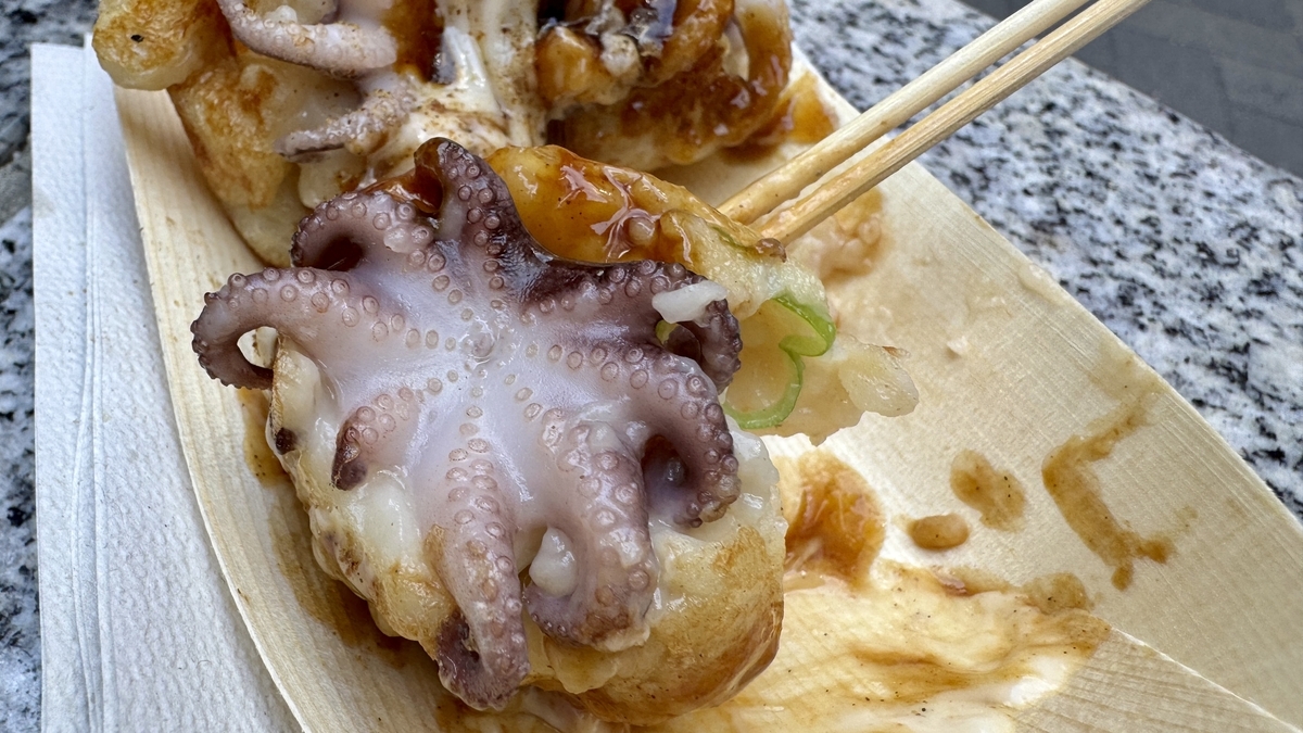 たこ焼きの上にイイダコが丸ごと乗った一玉を箸で持ち上げたアップ