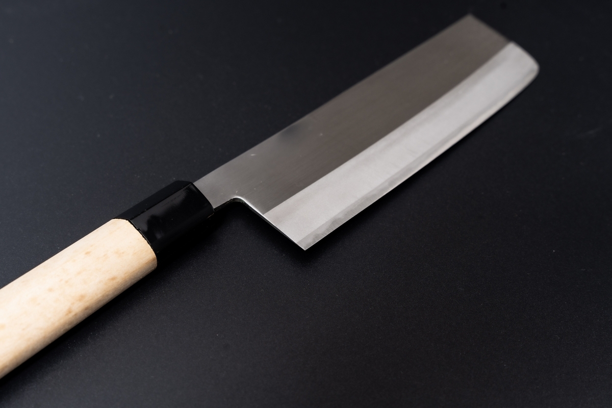 黒い背景に置かれた菜切り包丁の四角い刃と白木の柄