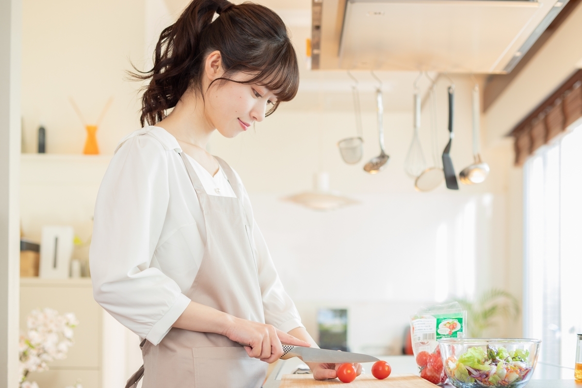 明るいキッチンでエプロン姿の女性が包丁でミニトマトを切る様子