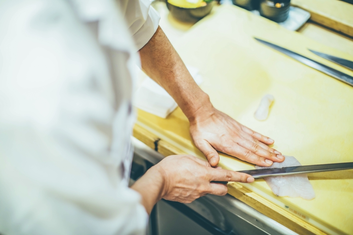 黄いろいまな板の上で包丁を使って魚の切り身を切る職人の手元