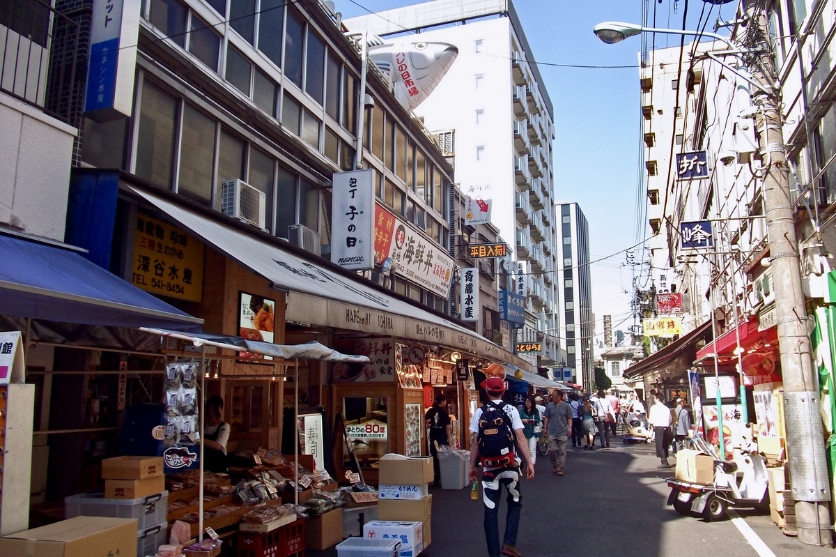 築地場外市場の通りに並ぶ店舗の看板と軒先の品物を眺めながら歩く観光客