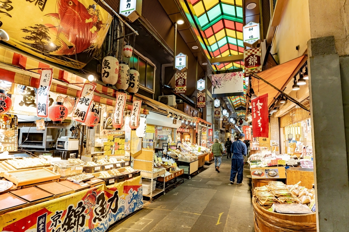 錦市場のアーケードに連なる提灯と食材店の店先を歩く観光客